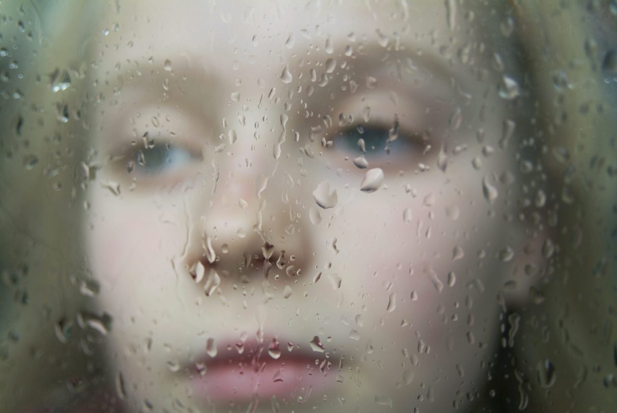 Girl looking out a window with gentle rain falling